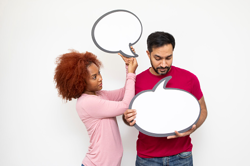 Communicating couples concept: Mid-adult man and a young woman holding blank speech bubbles for your message. It appears as though the man is talking. They both have serious expressions.