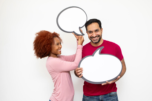 Communicating couples concept: Mid-adult man and a young woman holding blank speech bubbles for your message. It appears as though the man is talking. They both have cheerful and happy expressions.