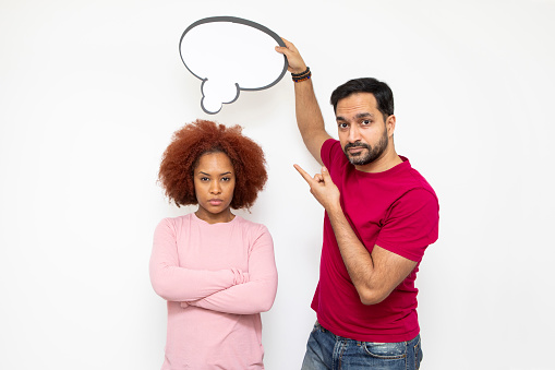 Couples with ideas and making decisions concept: Mid-adult man holding a blank thought bubble for your message above a young woman. They both have doubtful expressions.