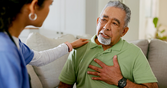 Nurse, senior man and talk of chest pain, heart problems and discomfort in consultation at home. Medical caregiver, elderly male patient and worry of cardiovascular lung fail or hypertension