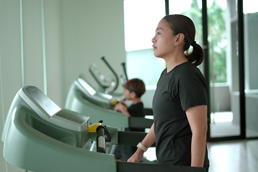 Woman and a boy run on a treadmill, exercising.