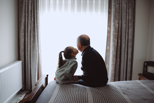 Little cute girl and her grandfather are spending time together at home. Having fun, hugging and smiling while sitting on bed