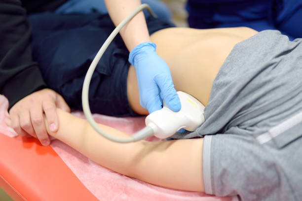 Doctor making abdominal ultrasound for boy using scanner machine. Female doc runs ultrasound sensor over patient tummy. Mother supports son during diagnosis examination of internal organs Doctor making abdominal ultrasound for boy using scanner machine. Female doc runs ultrasound sensor over patient tummy. Mother supports son during diagnostic examination of internal organs 15495 stock pictures, royalty-free photos & images