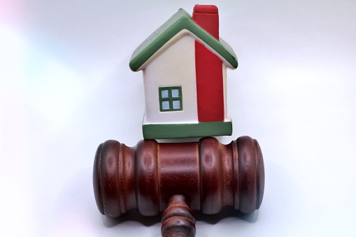 House model, hammer judge gavel on wooden table with white wall background. Foreclosure, bankruptcy concept. Person is unable to repay outstanding debts or obligations, stops mortgage payment.