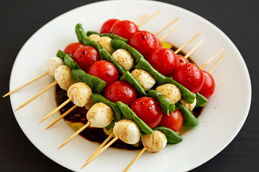 Homemade caprese skewer appetizer on a plate on a black surface, side view.