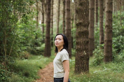 Young Asian woman stepping on a forest trail and looking up, enjoying the nature