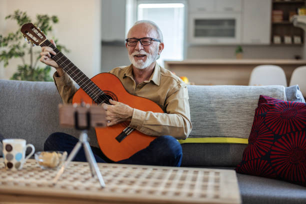 istock Bearded senior man playing on guitar shooting music video or tutorial on modern smartphone at home studio. Senior man shooting music video. 2022328289