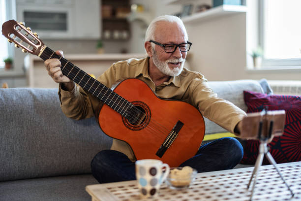 istock Bearded senior man playing on guitar shooting music video or tutorial on modern smartphone at home studio. Senior man shooting music video. 2022328812