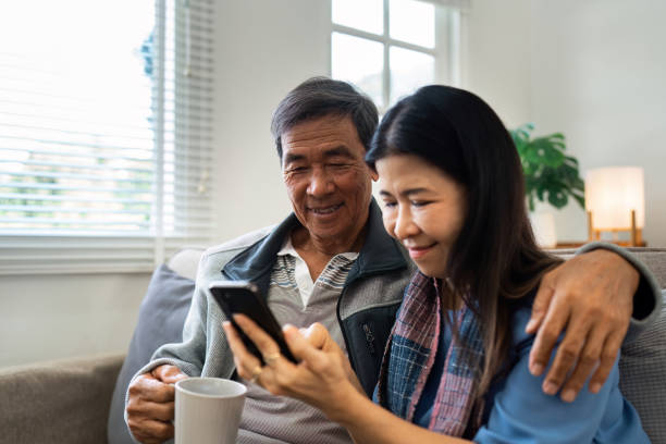 istock Retired elderly couple sits on couch drink tea and using mobile together and relax in their home. Senior Activity Concept 2022332503
