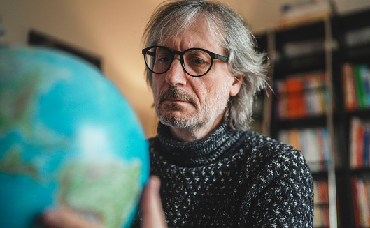a worried middle-aged man looks at a globe