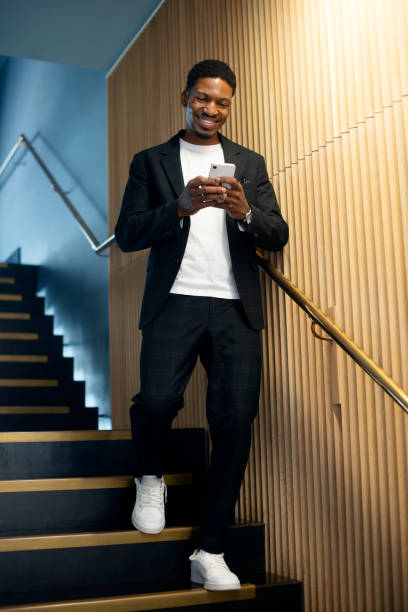 黒人男性、電話、ホテルの階段で笑顔でテキストメッセージを送ったり、読んだり、アプリで連絡先の通知を確認したりします。ニューヨークのブログ、チャット、ソーシャルネットワーク� - staircase walking office steps ストックフォトと画像