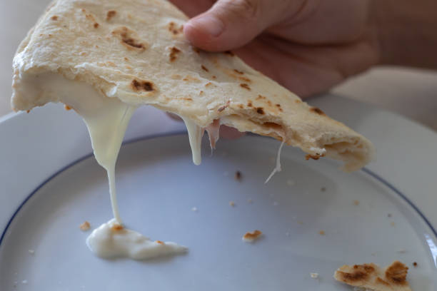 Hand Holding a Bitten Flat Bread Filled with Cheese and Ham on top of a Plate.