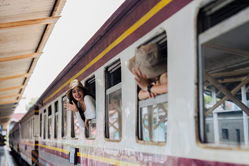Female tourists waving at each other at train window at train station. Concept of active lifestyle and travel.