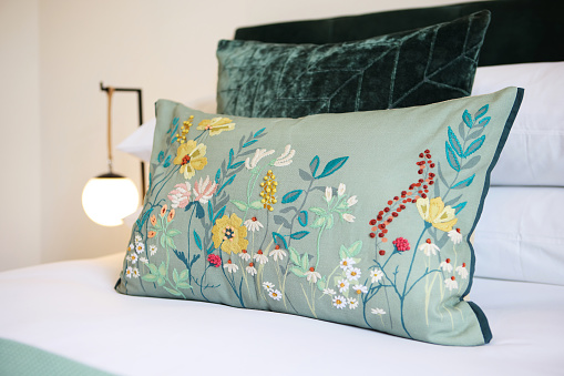 Home, decor and pillow on bed or upholstery flowers in apartment or creative stitching, decorations or interior design. Cushion, floral and cozy environment or house furniture, accommodation or hotel