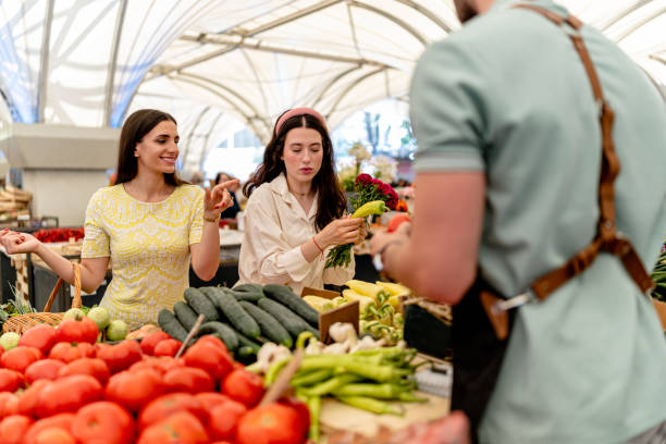 istock Two Women Engage in a Vibrant Vegetable Shopping Experience with a Friendly Vendor 2022366847