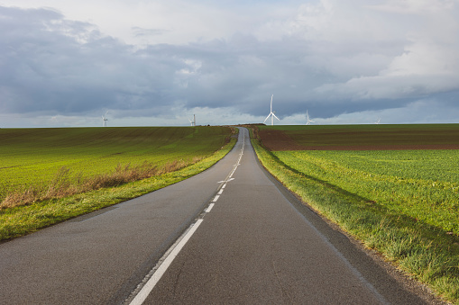 regional road with crops on the sides and wind energy mills in the background