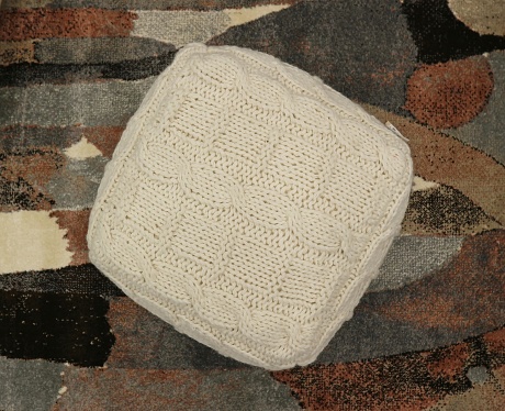 Square woolen white pouf on multicolored carpet background. Top view.