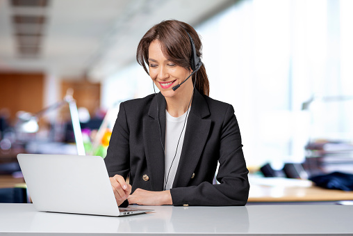 Customer service assistant wearing headset while sitting behind her computer and working in the call center. Copy space.
