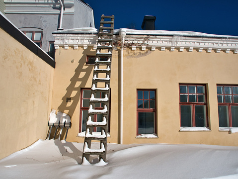 Wooden ladder against yellow wall in wintertime