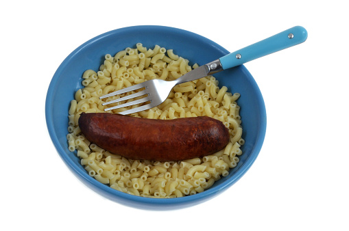 Smoked sausage and shellettes with butter on a plate with a fork close-up on a white background
