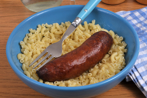 Smoked sausage and buttered shellettes on a plate with a fork close-up