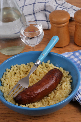 Smoked sausage and butter shellettes on a plate with a fork and a glass of water close-up