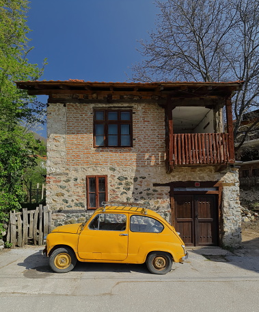 Classical orange-yellow, so-called Fikjo car from the former Yugoslav communist era stopped in front of a local house at the beginning of the trail going to the local springs. Vevcani-North Macedonia.