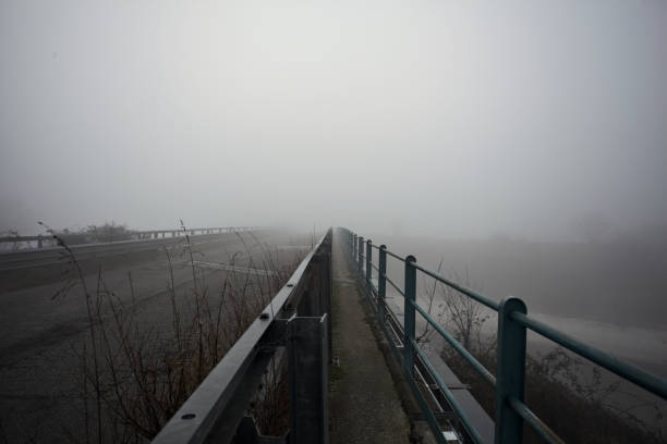 Bridge with pavement and railing over a river in the italian countryside on a foggy day