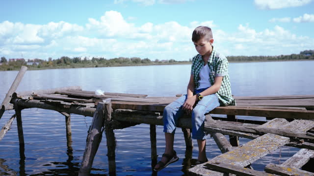 Solitude by the Lake: Sad Boy Contemplating Life on the Pier Amidst Sunny Weather
