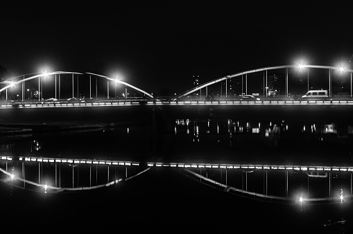 A monochrome image of a bridge over water in the night