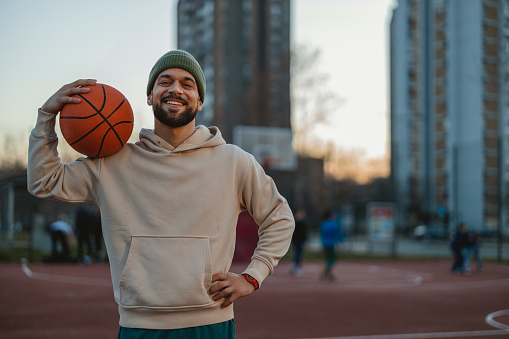 Smiling Mid Adult Basketball Player Looking at Camera While Playing Basketball Outdoors at Dusk