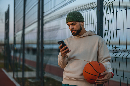 Night Portrait Male Basketball Player Using Smartphone on Basketball Court. Sport, Active Lifestyle Concept.