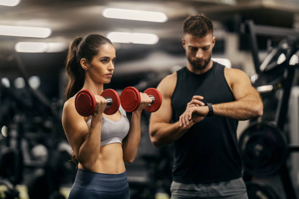 istock A strong sportswoman is doing biceps curls with dumbbells while her trainer is measuring time in a gym. 2022454580