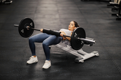 A fit sportswoman is working out with barbell on a bench.