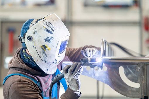 A welder welding two pieces of metal together in a metal fabrication facility.