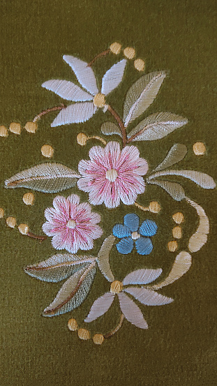 closeup of a composition of flowers and leaves embroidered on a green background