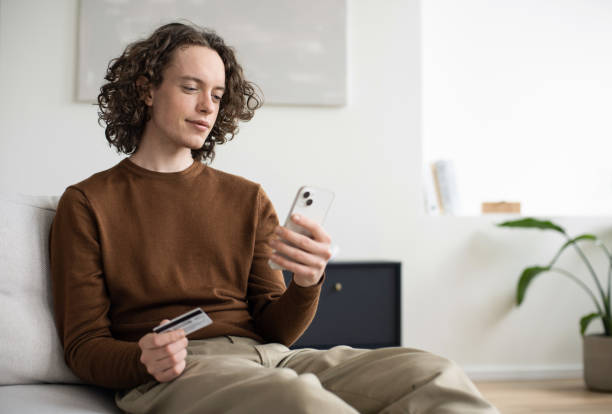 istock Payment online. Young man using smartphone and paying with credit card at home 2022485421