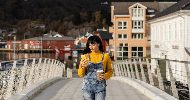femme écoutant de la musique avec des écouteurs et buvant du café à emporter dans la rue d’une ville norvégienne - norwegian culture photos et images de collection
