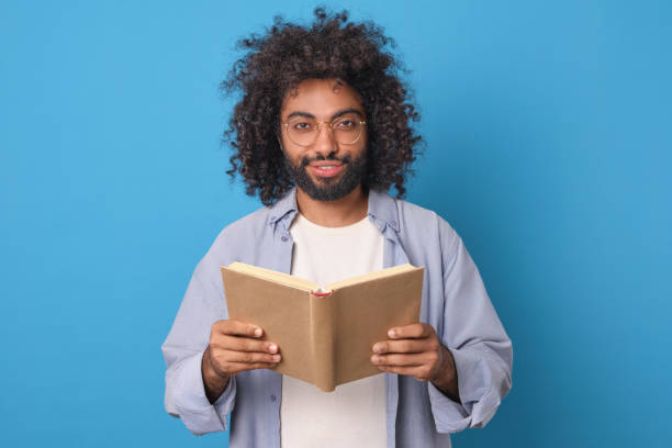 istock Young happy ethnic Arabian man with open book in hands stands in studio 2022498119