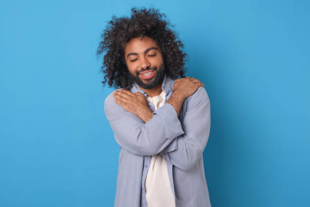 istock Young optimistic positive Arabian man hugs himself by shoulders stands in studio 2022501257