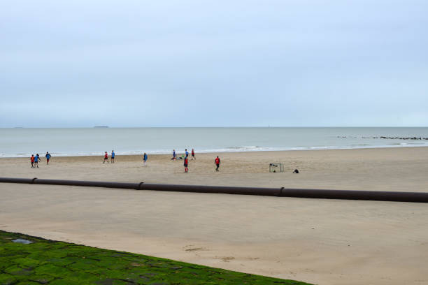 Blankenberge, West-Flanders, Belgium - February 17, 2024: male football players, red against blue shirts playing football on the wet sand in front of the sea during crocus leave