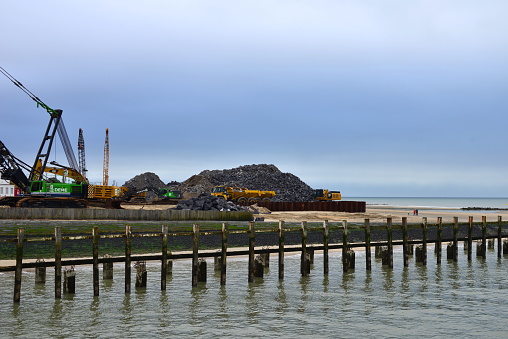 Blankenberge, West-Flanders, Belgium - February 17, 2024: To prevent the blowing sand from silting up in the marina, a dike is being built. Vehicles trucks, bulldozers Volvo ECR 380, Komatsu HM 400