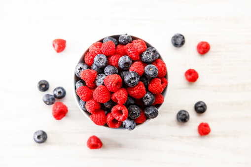 Mix of ripe berries. Blueberries and raspberries in bowl on wooden background.