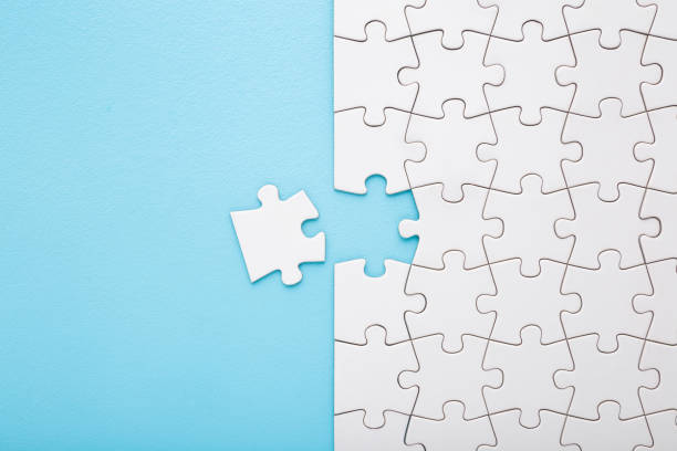 istock Unfinished white puzzle with last one piece on light blue table background. Pastel color. Closeup. Top down view. 2022520933