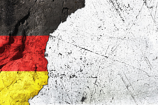 German national flag on cracked, roughly plastered wall with white copyspace.