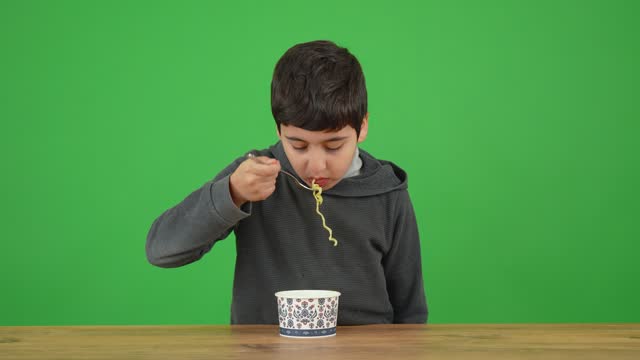 An eight-year-old boy happily eating a plate of noodles