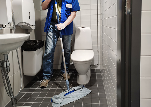 A male janitor cleans a public toilet and washes the floor. Cleaning service.