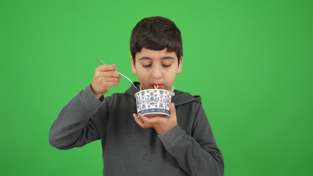 An eight-year-old boy holds a bowl of noodles and eats it happily