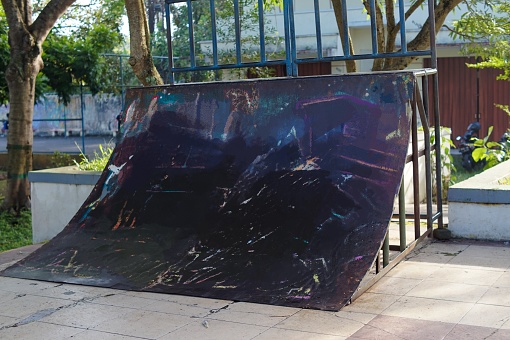 A black concave obstacle board for skateboarders in a city park.