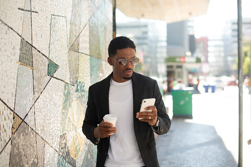 Smartphone, city and business black man with coffee for social media, networking or communication. Professional, urban town and African person with phone for online chat on commute, walking or travel